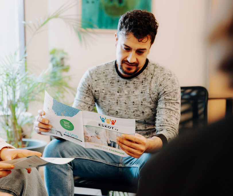 Istuva henkilö pitää kädessään esitettä, jossa on Eskot ry:n logo.